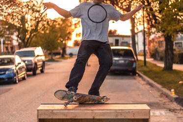 Young male skateboarder balancing on top of ramp on suburban street at sunset, neck down - ISF19817