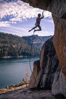 Junger männlicher Kletterer, der an einem Seil von einer Felswand baumelt, High Sierras, Kalifornien, USA - ISF19840