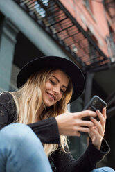 Frau schaut lächelnd auf ihr Handy und schreibt eine SMS, New York, USA - ISF19849