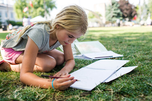 Girl sitting on grass doing homework - ISF19864