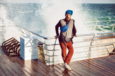 Hipster against railing, sea splash in background - ISF19989