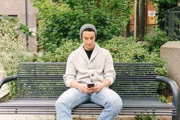 Young man texting while sitting on bench, Vancouver, Canada - ISF20004