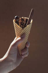 Woman's hand holding ice cream cone with autumnal filling - MOMF00525