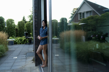 Frau steht auf der Terrasse eines modernen Hauses und hält einen Becher - HHLMF00555