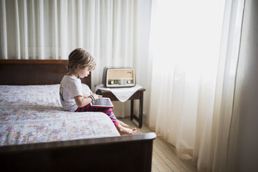 Junge sitzt auf dem Bett und benutzt ein Tablet - AZOF00080