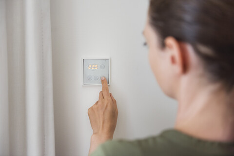 Frau benutzt Smart-Home-Schalter an der Wand, lizenzfreies Stockfoto