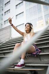 Young woman sitting on stairs, using smartphone - RAEF02154