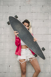 Portrait of a young woman with her long board, in front of a wall - RAEF02168