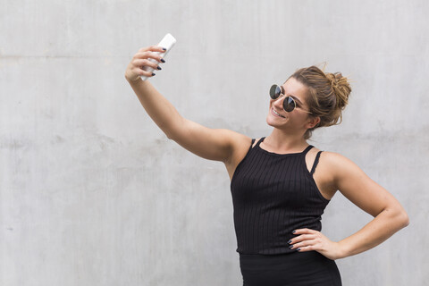 Porträt einer lächelnden, schwarz gekleideten jungen Frau, die ein Selfie mit ihrem Smartphone macht, lizenzfreies Stockfoto