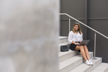 Lächelnde Geschäftsfrau, die auf einer Treppe sitzt und einen Laptop benutzt - JUNF01522
