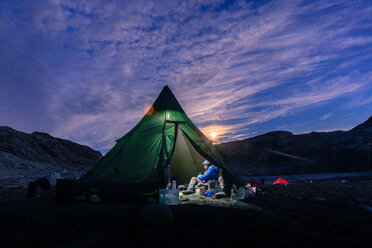 Man sitting in illuminated tent at sunset, Narsaq, Vestgronland, South Greenland - CUF46095