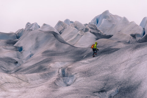 Männlicher Wanderer wandert über graue, schneebedeckte Landschaft, Narsaq, Vestgronland, Südgrönland, lizenzfreies Stockfoto