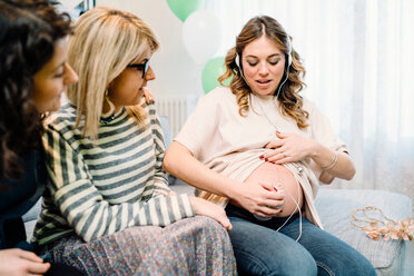 Pregnant woman and friends on sofa using prenatal listening device - CUF46128
