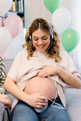 Pregnant woman on sofa using prenatal listening device - CUF46136