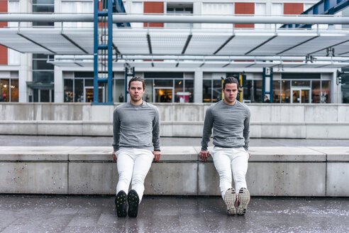 Junge männliche Zwillinge machen umgekehrte Liegestütze gegen die Wand in der Stadt - CUF46156