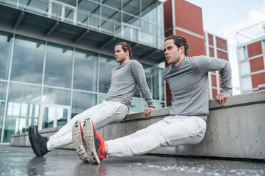 Young male twins doing reverse push ups against wall in city, full length - CUF46157