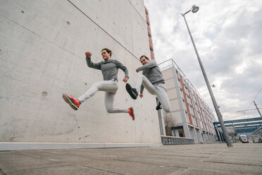 Junge erwachsene männliche Zwillingsläufer, die mitten in der Luft auf dem Bürgersteig der Stadt laufen und springen - CUF46174