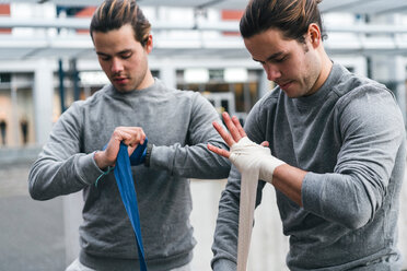 Identical male adult twin boxers training outdoors, bandaging hands with hand wraps - CUF46178