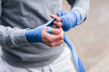 Young male boxer training outdoors, bandaging hands with hand wraps, mid section - CUF46179