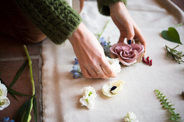 Frau arrangiert pastellfarbene Blütenköpfe und Blattstiele auf Textil, Detail der Hände - CUF46280