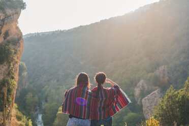 Spain, Alquezar, rear view of two young women on a hiking trip sharing a blanket - AFVF01790