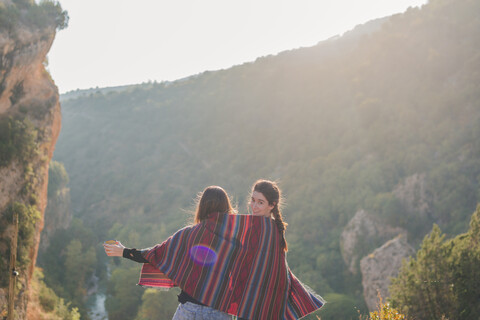 Spanien, Alquezar, Rückansicht von zwei jungen Frauen auf einer Wanderung, die sich eine Decke teilen, lizenzfreies Stockfoto