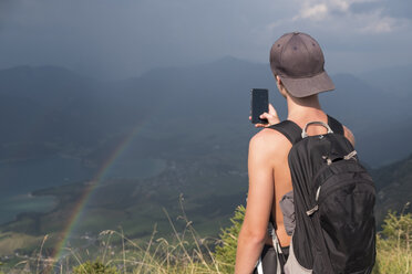 Austria, Salzkammergut, Mondsee, teenage boy taking a scenic picture with rainbow - HAMF00424