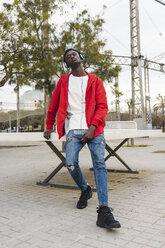 Cool young man with headphones sitting outdoors, listening music - AFVF01812