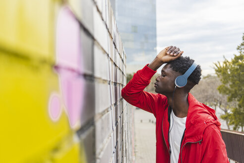 Young black man leaning on wall, listening music with headphones - AFVF01814