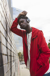 Young black man leaning on wall, listening music with headphones - AFVF01815