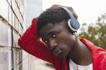 Junger schwarzer Mann lehnt an der Wand und hört mit Kopfhörern Musik - AFVF01816