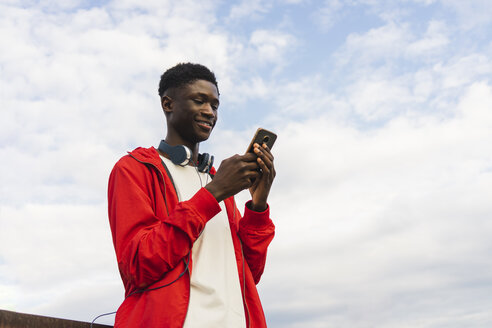 Junger Mann mit Kopfhörern, der Textnachrichten auf seinem Smartphone liest - AFVF01822