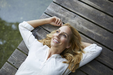 Lächelnde blonde Frau auf Holzsteg an einem See liegend - PNEF01012