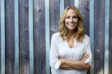 Portrait of smiling blond woman in front of wooden wall - PNEF01017