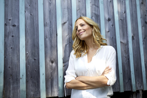 Smiling blond woman in front of wooden wall stock photo