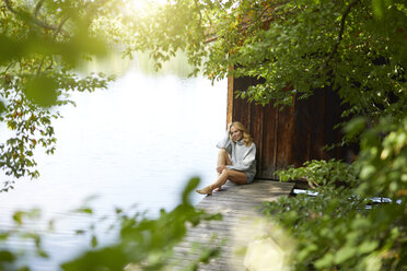 Entspannte Frau sitzt auf einem Holzsteg an einem abgelegenen See - PNEF01026