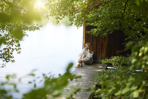 Entspannte Frau sitzt auf einem Holzsteg an einem abgelegenen See, lizenzfreies Stockfoto