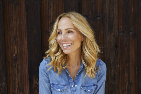 Happy blond woman in front of wooden wall - PNEF01049