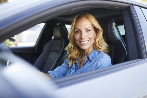 Portrait of smiling woman driving car looking out of window stock photo