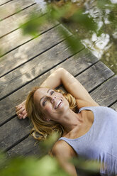 Happy blond woman lying on wooden jetty at a lake - PNEF01066