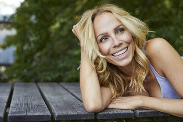 Porträt einer glücklichen blonden Frau, die auf einem Holzsteg liegt - PNEF01080