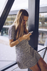 Attraktive junge Frau in einem Kleid mit Leopardenmuster, die ihr Mobiltelefon überprüft - RSGF00024