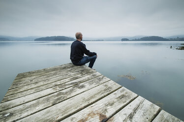 Einsamer Mann sitzt auf einem Steg und schaut in die Ferne - RAEF02179