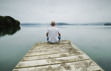 Back view of man sitting on jetty looking at distance - RAEF02180