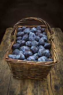 Wicker basket of organic plums, wooden table - LVF07461