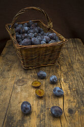 Wicker basket of organic plums, wooden table - LVF07463