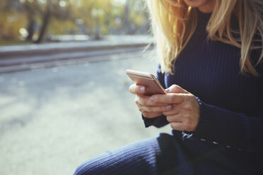 Hände einer blonden Frau mit Smartphone in einem herbstlichen Stadtpark - AZF00099