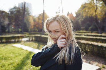 Porträt einer verspielten blonden Frau im herbstlichen Stadtpark - AZF00102