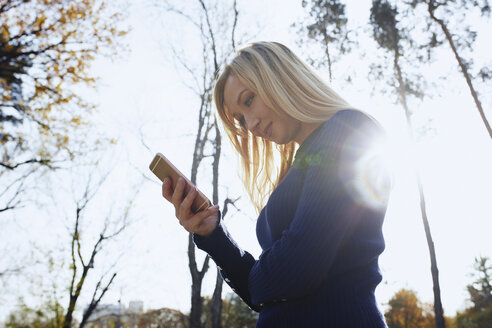 Lächelnde blonde Frau mit Smartphone im herbstlichen Park - AZF00104