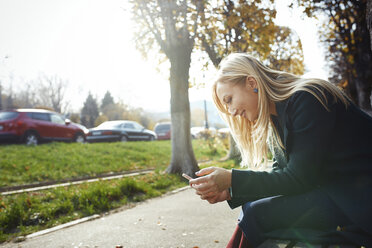 Lächelnde blonde Frau benutzt Smartphone im Freien - AZF00107